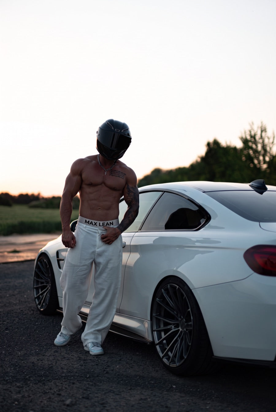 Fahrer mit Integralhelm vor weissem Coupe im Abendlicht, grauer MAX-LEAN-Bund ueber weiter Hose